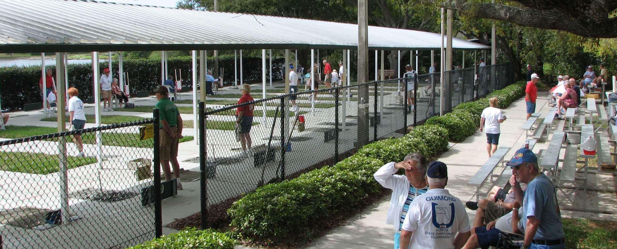 Rows of covered horseshoe courts beside the lake at Ed Wright Park, players and spectators on tournament day